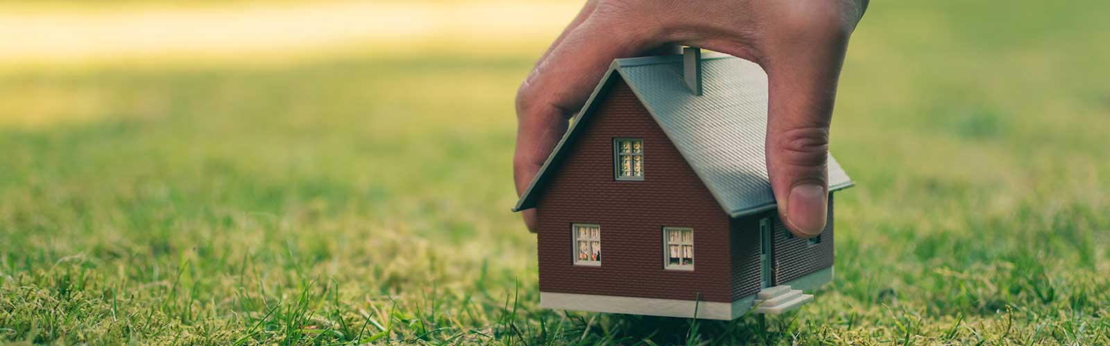 a hand holding a model of a house header image