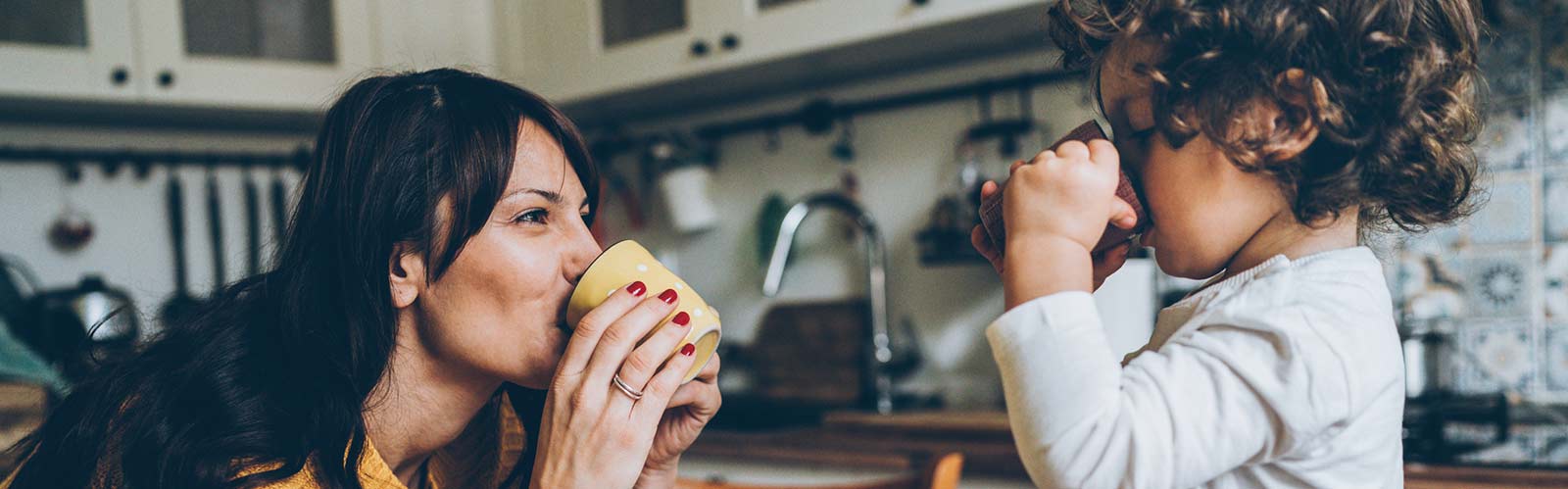 a mother and child drinking from a cup in a kitchen